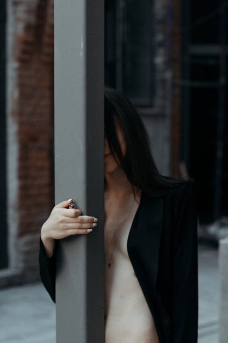 A mysterious portrait of a woman partially hidden behind a pole in an urban setting.